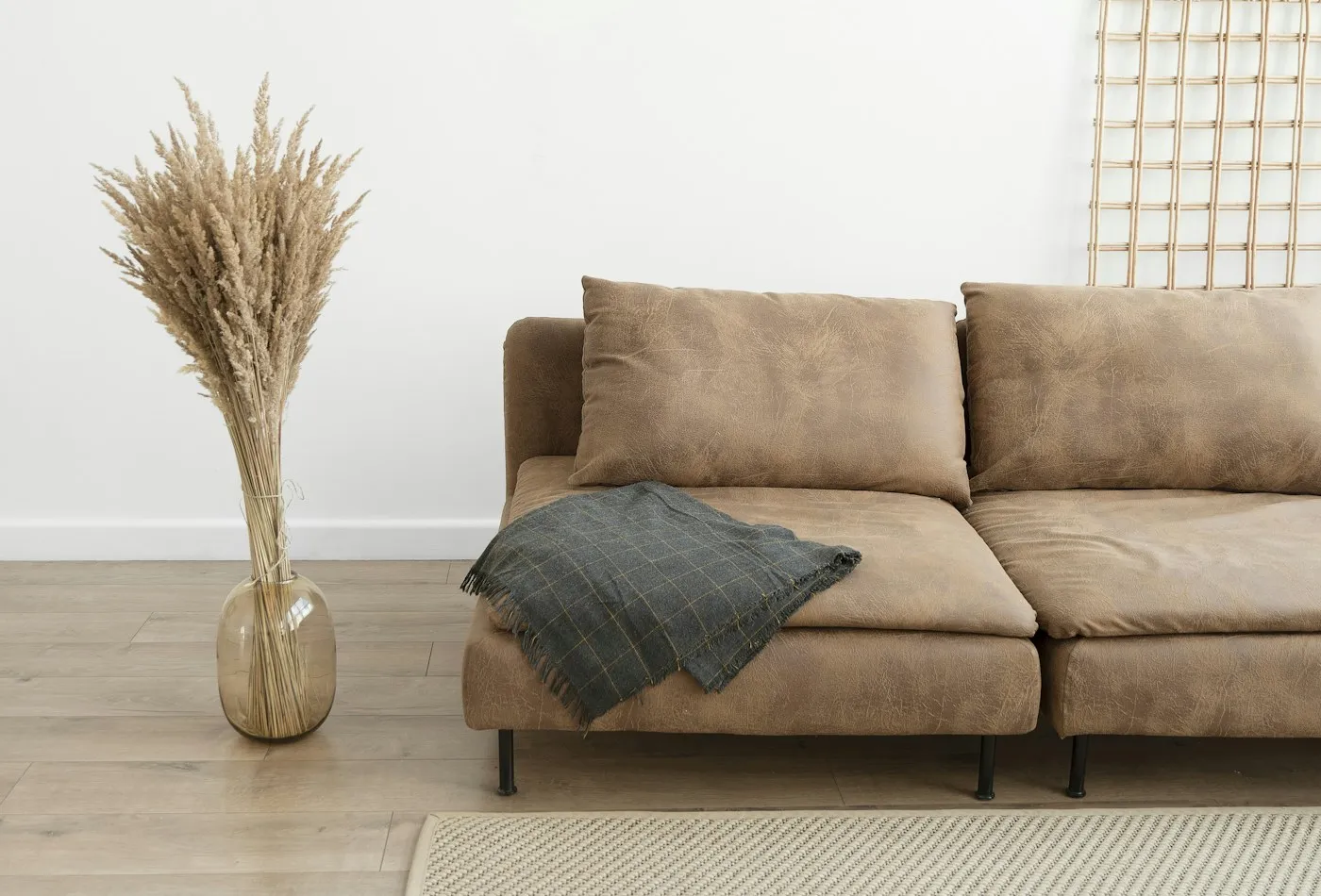 Brown modular sectional sofa with a gray throw beside a vase of dried grasses