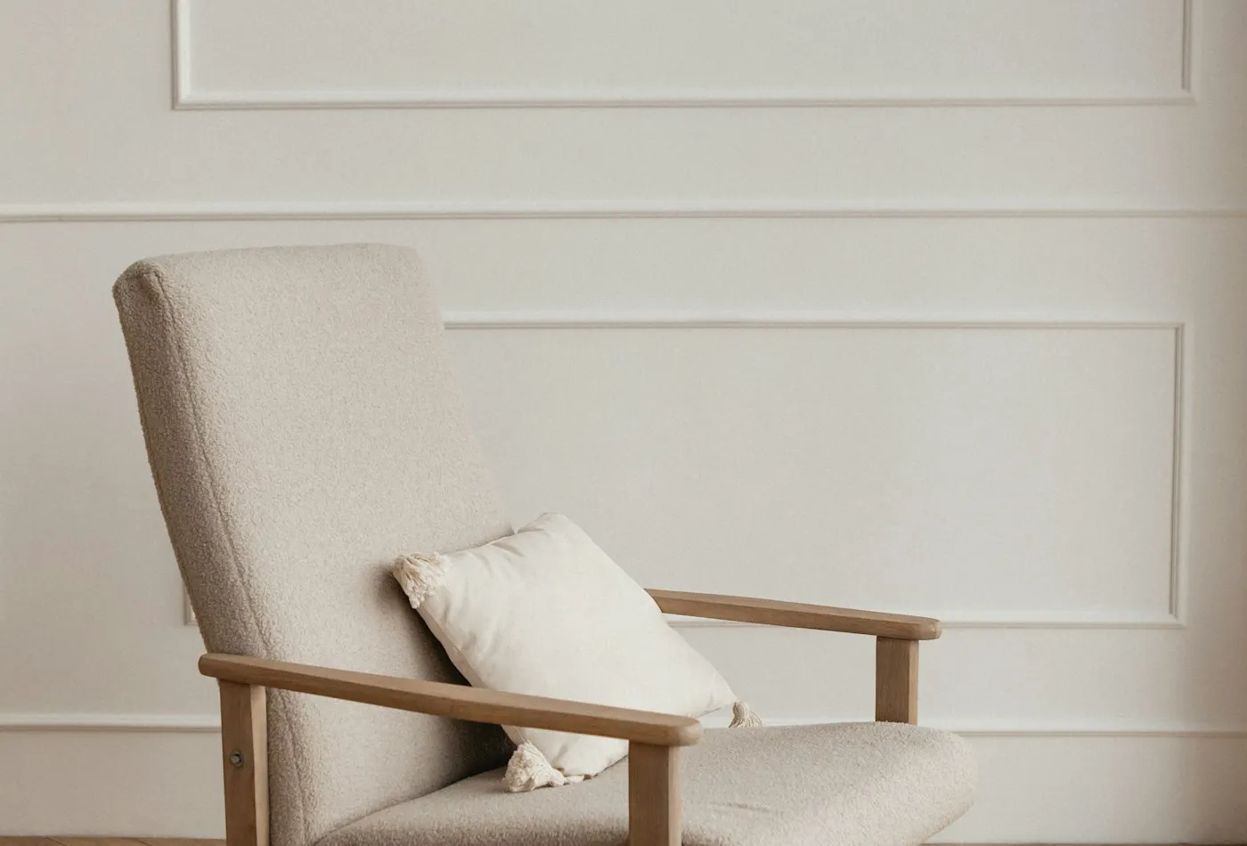 White upholstered accent chair with natural wood arms beside a paneled wall